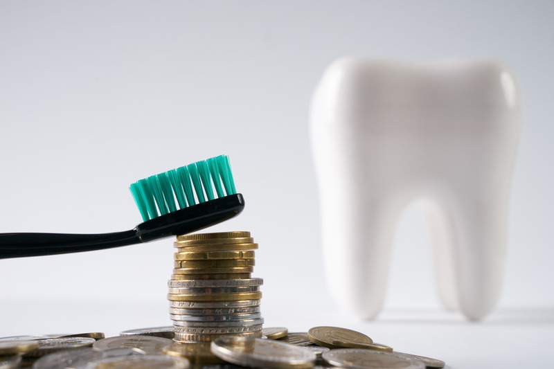 Stack of money next to a dentist model of a tooth