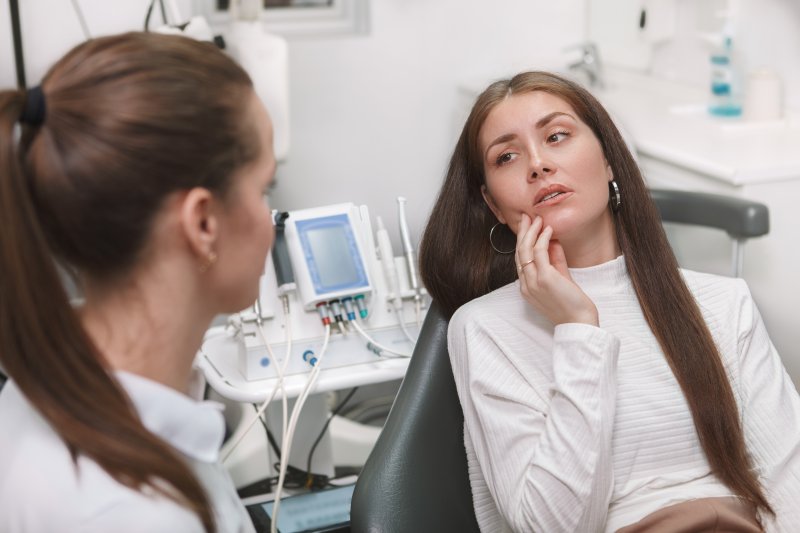 Patient holding cheek at dentist due to tooth sensitivity